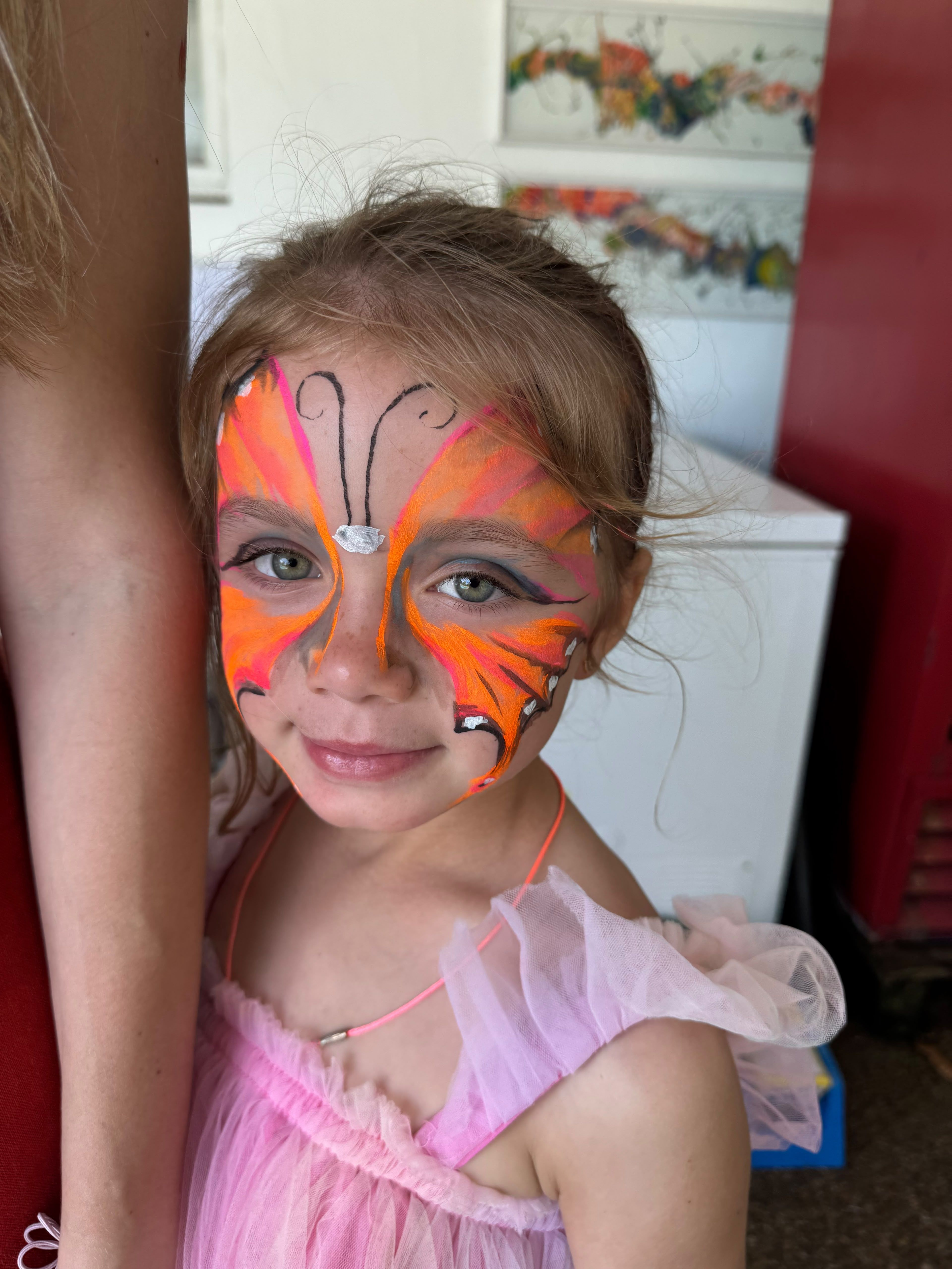 A girl with a pink and orange butterfly painted on her face